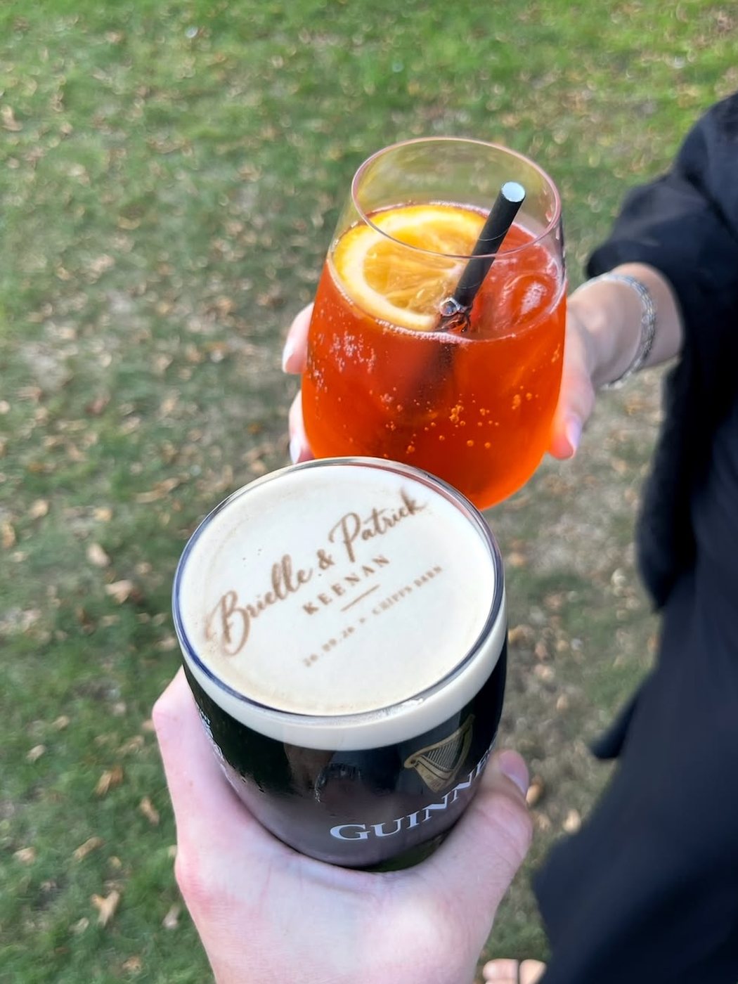 Bride and groom's names in script lettering printed on a pint of Guinness, held up next to an Aperol spritz at a wedding